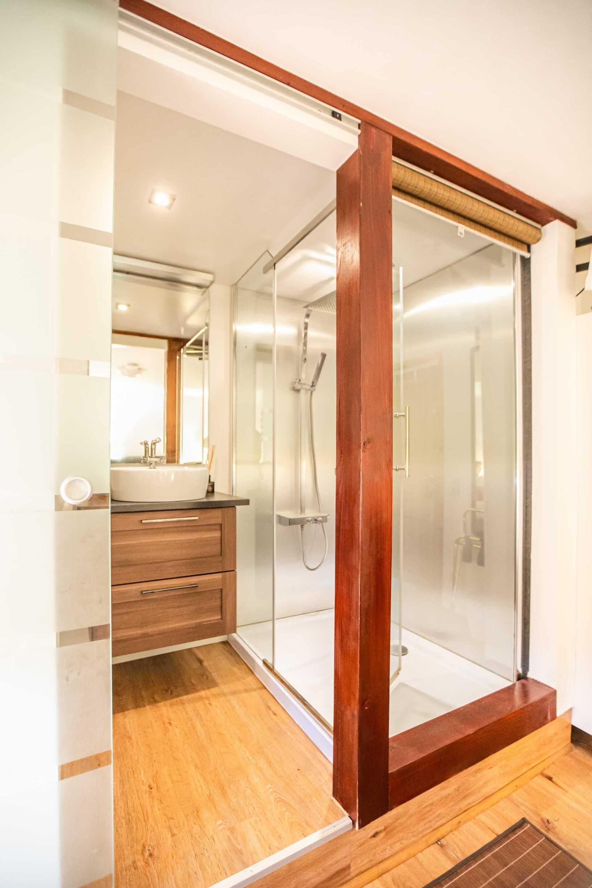 A modern bathroom with a glass-enclosed shower, wooden vanity, and a large mirror.