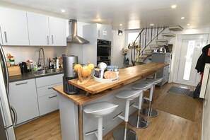 A modern kitchen with a central island, bar stools, a built-in oven, and a stainless steel sink. - Pension Schwedenkreuz (Reimerath)