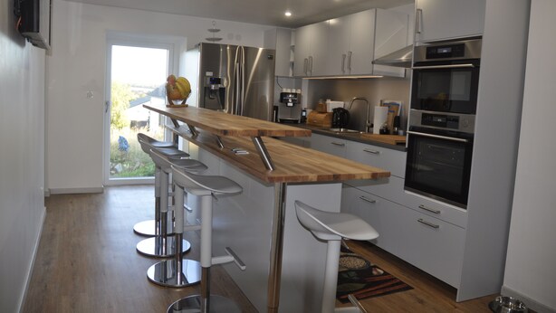 A modern kitchen with stainless steel appliances, a wooden bar counter, and three bar stools. - Pension Schwedenkreuz (Reimerath)