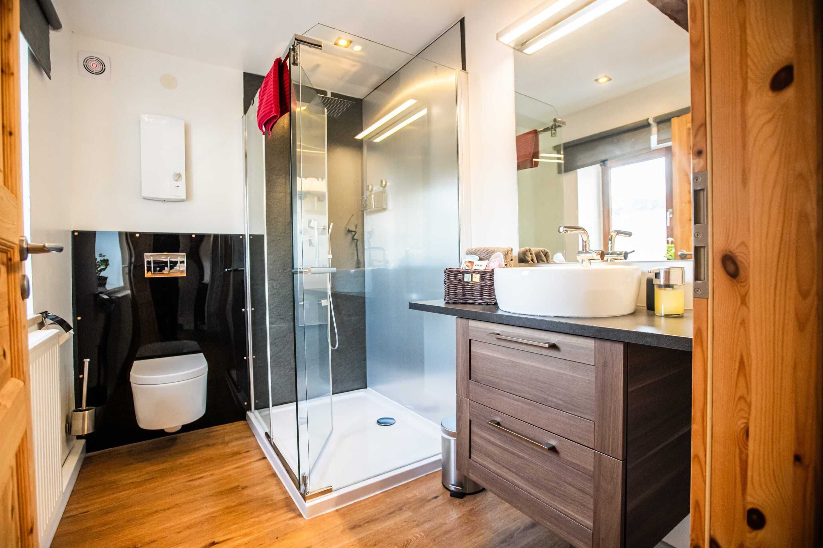 Un baño moderno con cabina de ducha de vidrio, tocador de madera y un espejo grande.