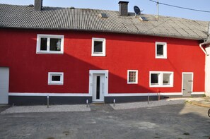 A red building with multiple windows and a door, a garage, and a gravel driveway. - Pension Schwedenkreuz (Reimerath)