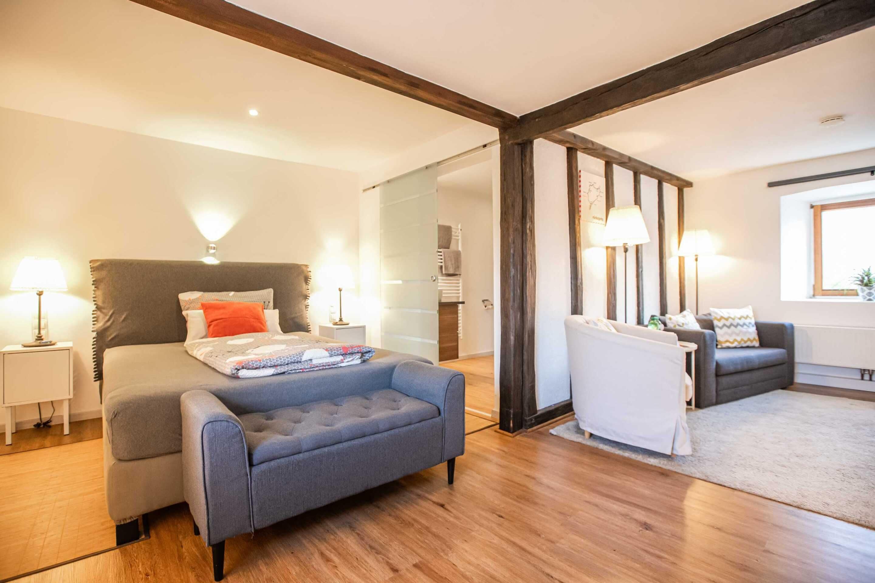 Un dormitorio moderno con cama, un sillón gris, un sofá y una ventana.