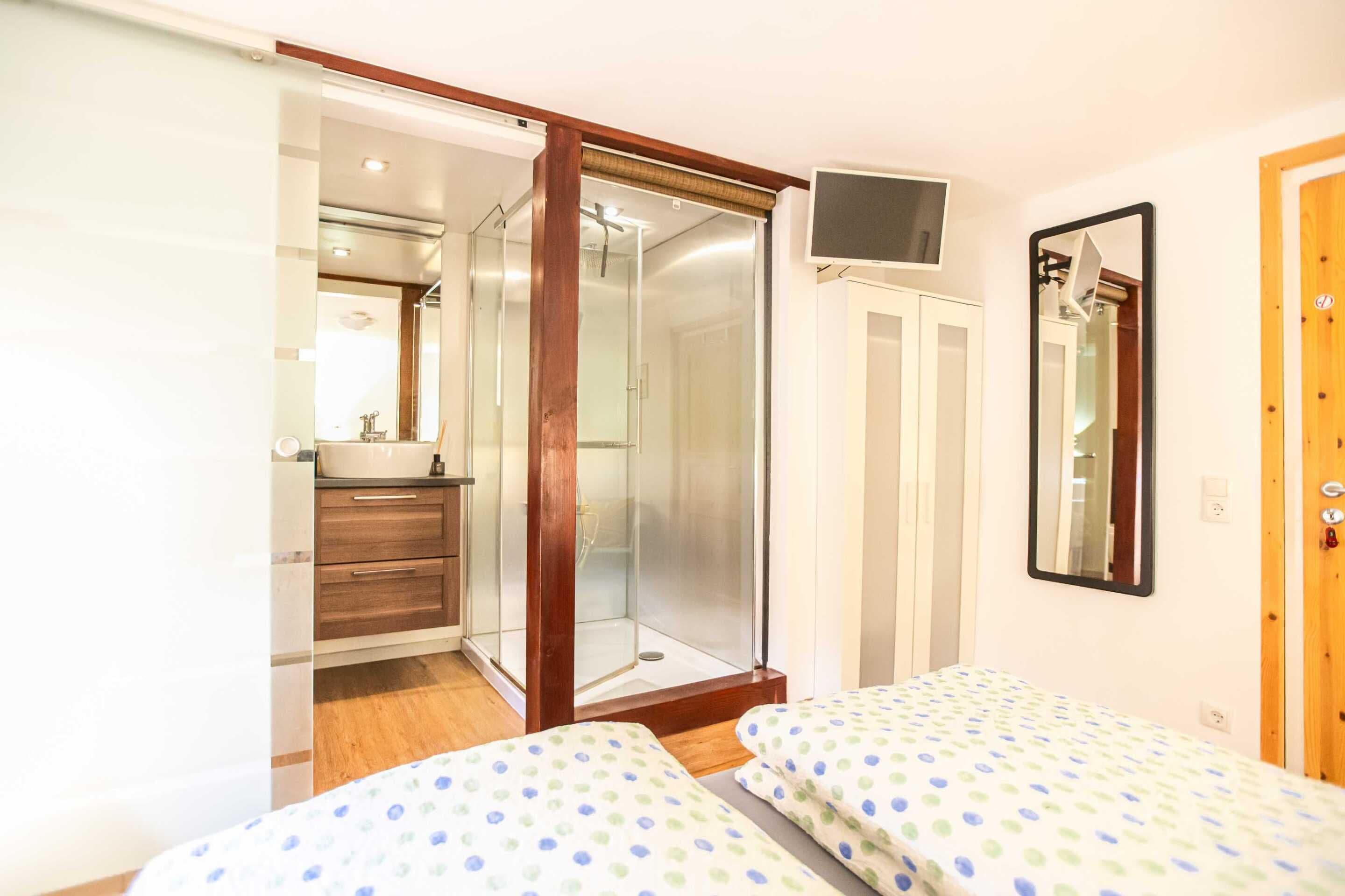A bedroom with two beds, a shower, a mirror, and a TV.
