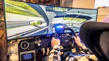 Una persona conduciendo un simulador de carreras equipado con un volante y una pantalla grande que muestra una escena de conducción.