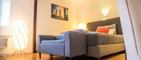 Un dormitorio moderno con un sofá gris, una mesita de noche con una lámpara y un cuadro en la pared.