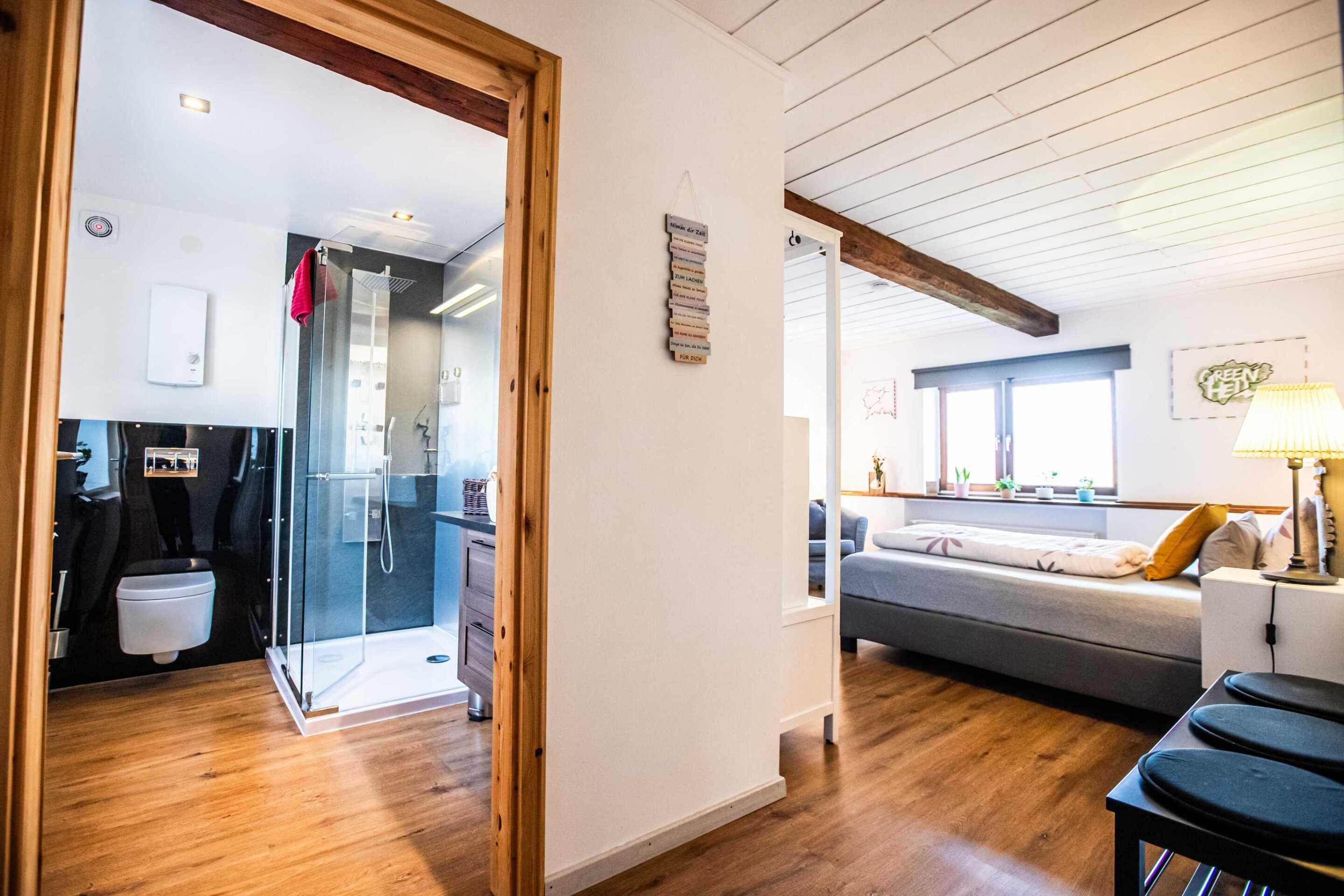 Ein modernes Interieur mit Holzboden, einer Glasdusche, einem grauen Sofa und einem kleinen Tisch mit Lampe.