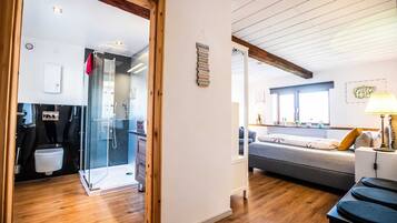 Ein modernes Interieur mit Holzboden, einer Glasdusche, einem grauen Sofa und einem kleinen Tisch mit Lampe.