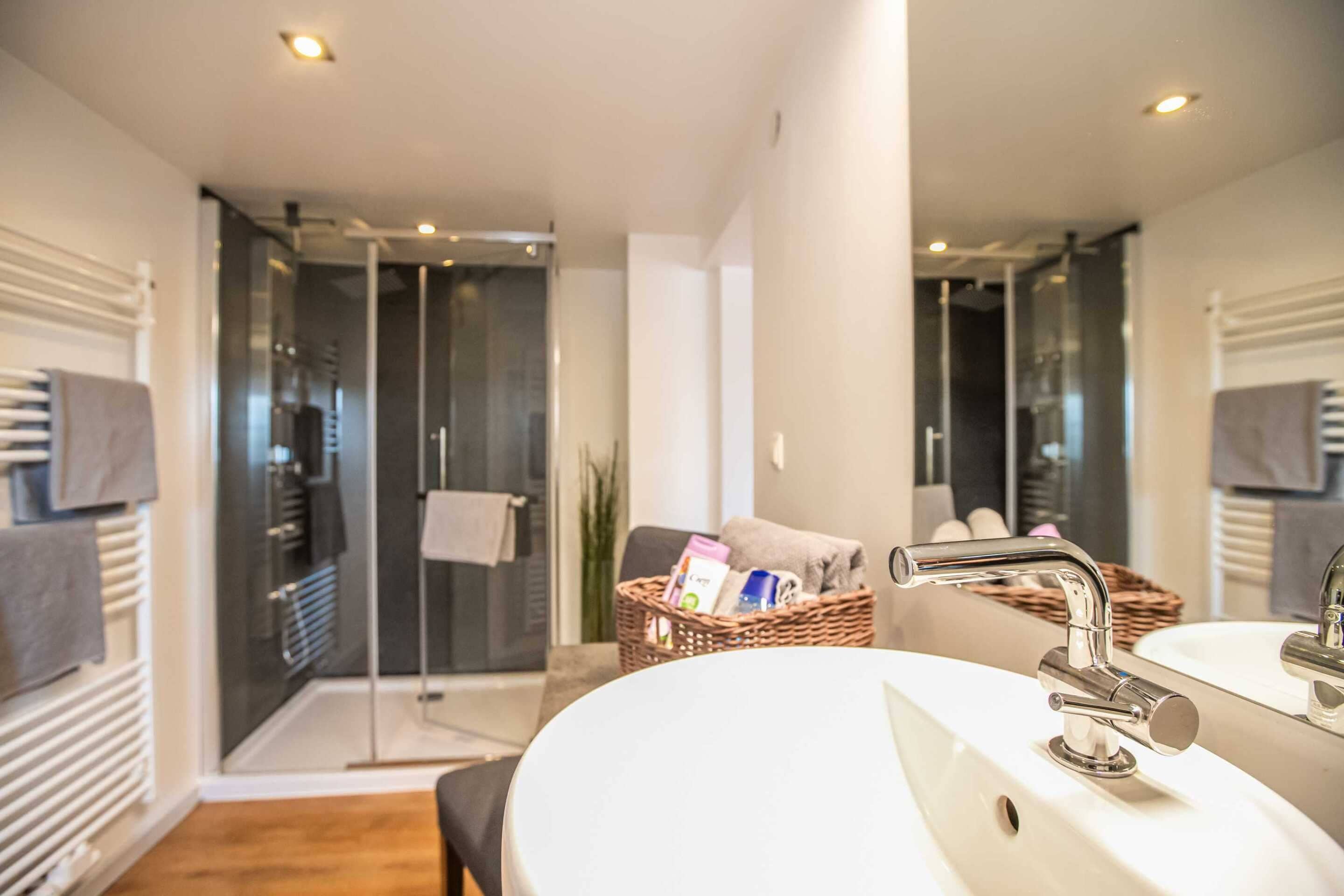 Une salle de bain moderne avec un grand lavabo blanc, une douche en verre et un panier en osier contenant des articles de toilette.