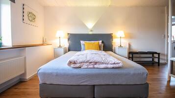 A bedroom with a bed, two bedside lamps, a nightstand, a window with a plant, and a radiator.