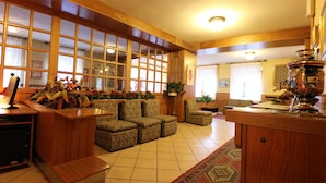 Um hall amplo com painéis de madeira, um balcão de recepção, assentos confortáveis e um vaso decorativo.