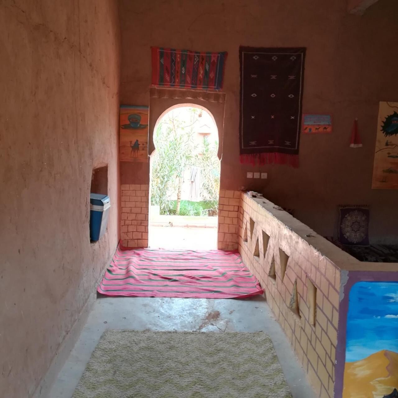 Un couloir étroit avec un mur en briques, une petite fenêtre et un tapis coloré.