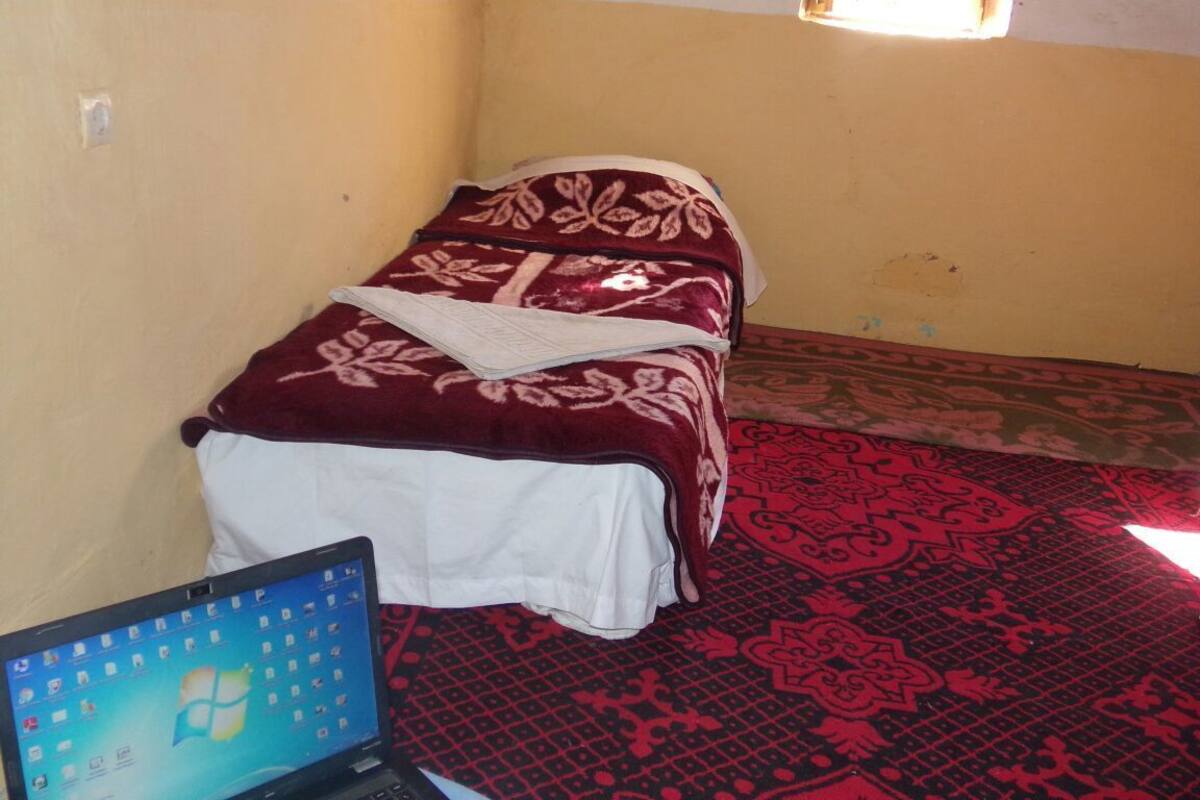 Ein kleines Zimmer mit einem Bett, einem Laptop auf dem Boden und einem gemusterten Teppich.