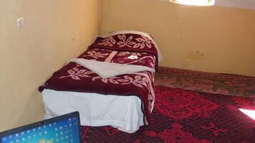 A small room with a bed, a laptop on the floor, and a patterned carpet.
