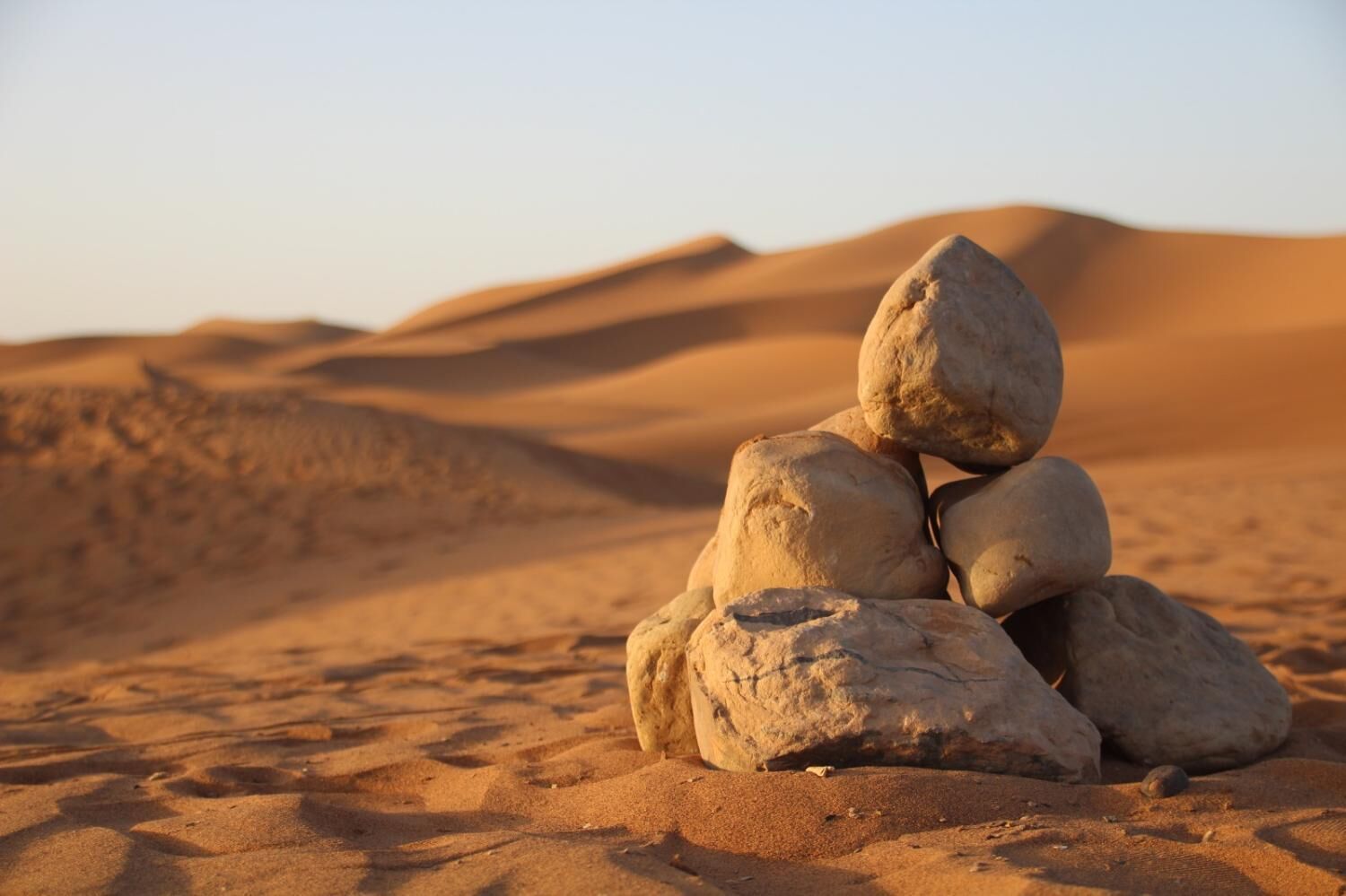 A stack of rocks in a desert with sand dunes in the background.