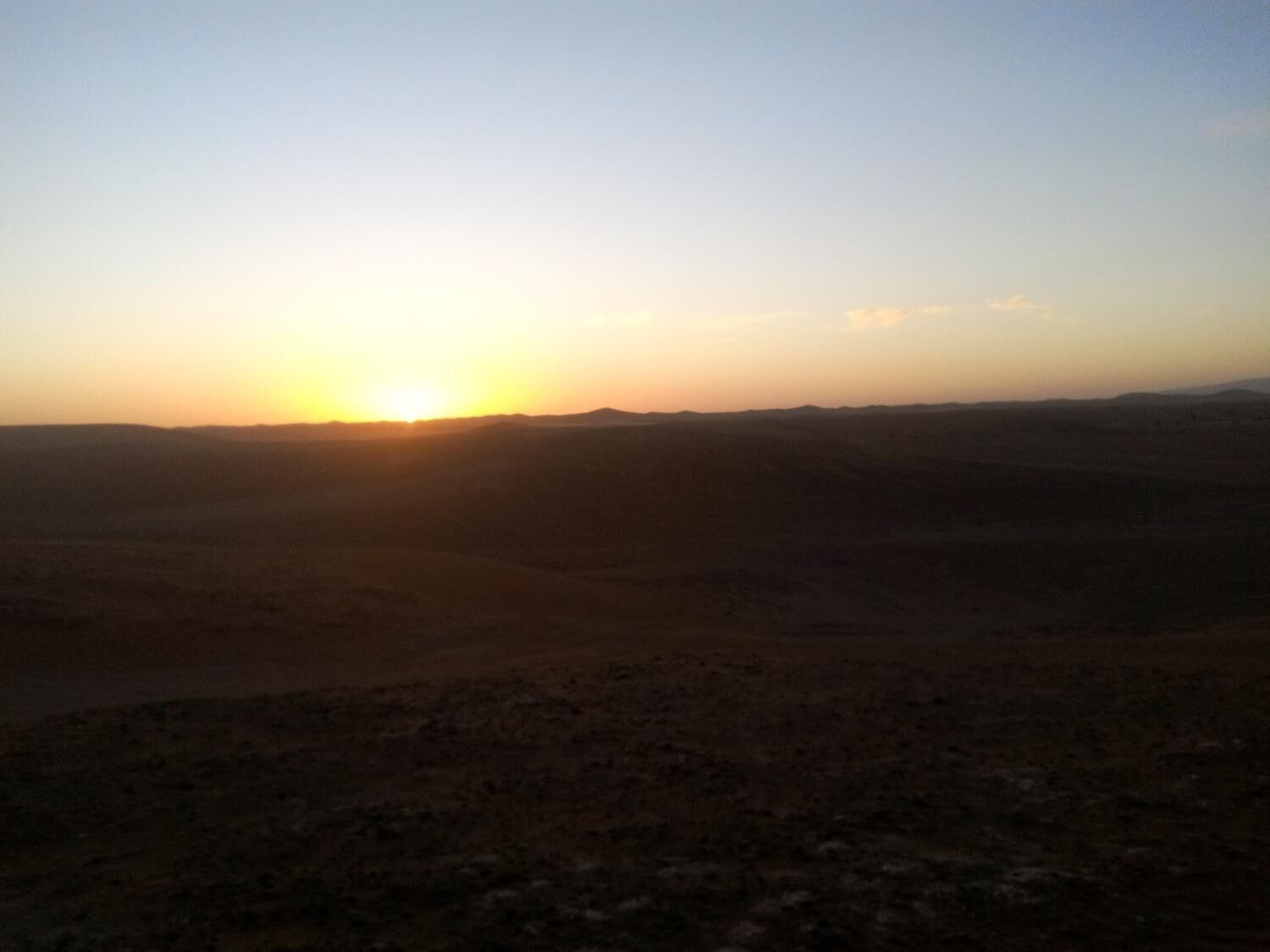 Paisaje desértico al atardecer con colinas onduladas en la distancia.