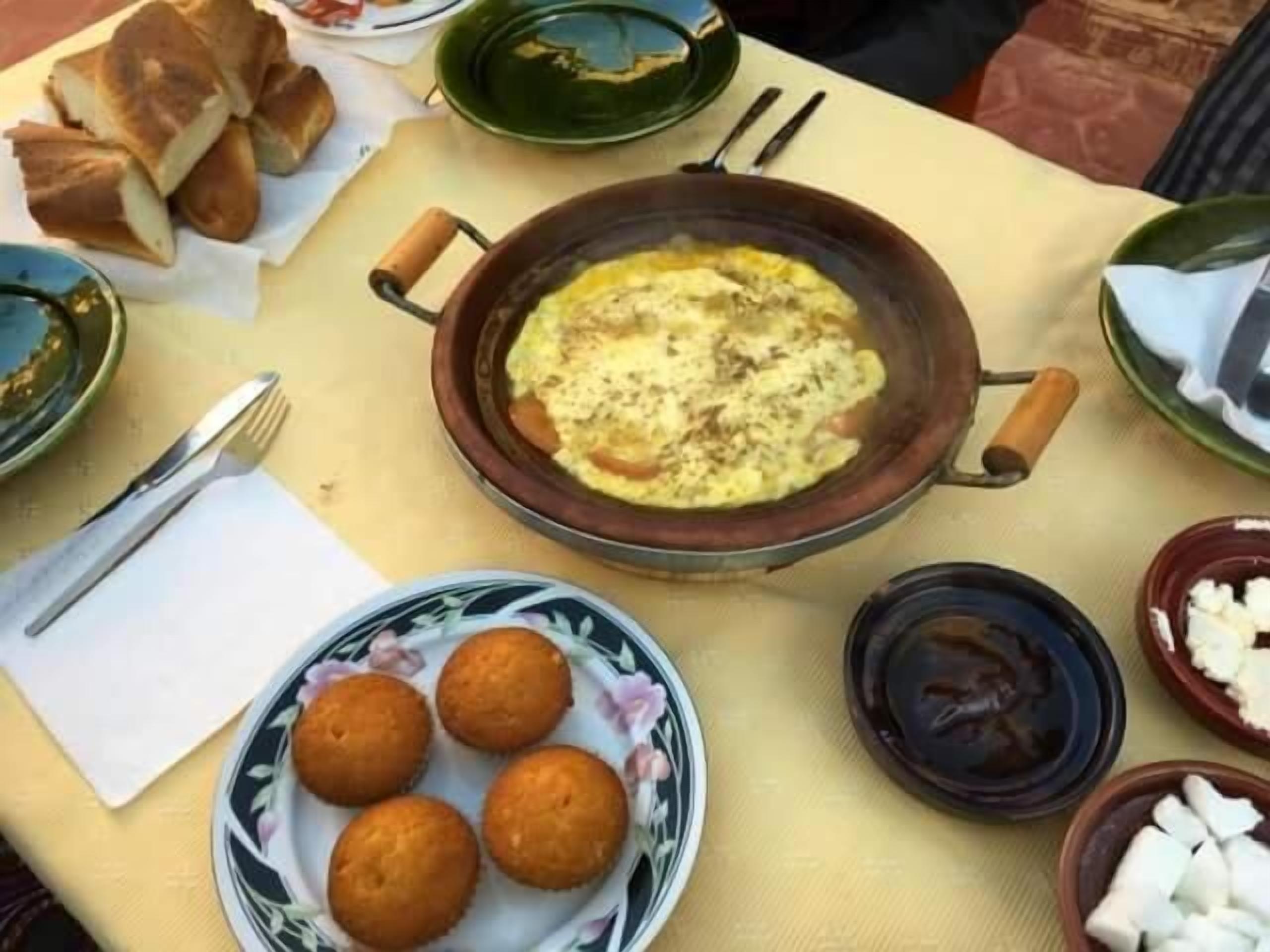 Una mesa con diversos platos, incluyendo una olla grande de comida, un plato de bollos redondos y varios cuencos con diferentes contenidos.