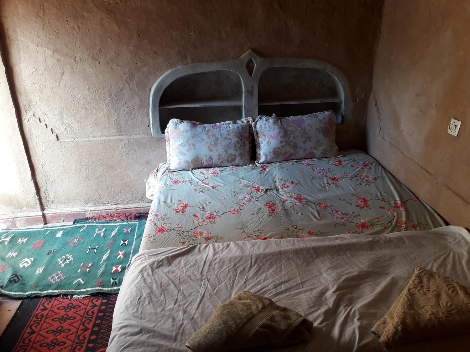 Una habitación con cama, colcha estampada, almohadas, cabecero y alfombra con diseño.