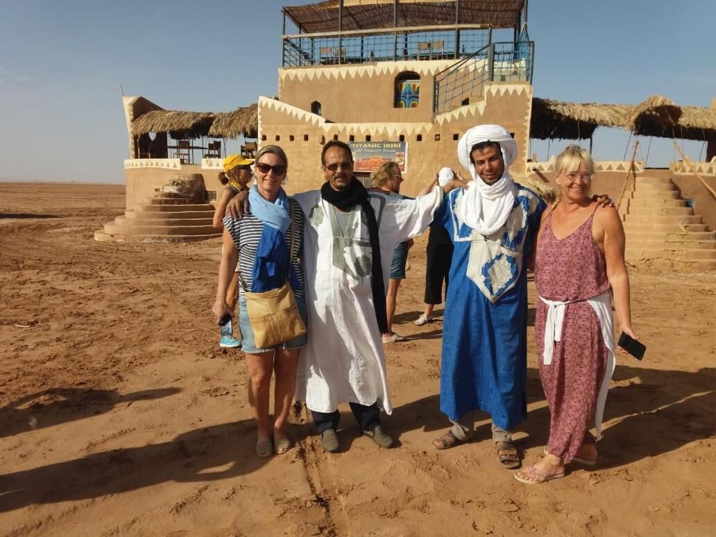 A group of people standing in a desert area with a building in the background.