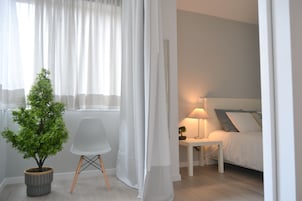 Quarto com cama, mesa de cabeceira com abajur, uma cadeira e uma pequena planta em vaso.