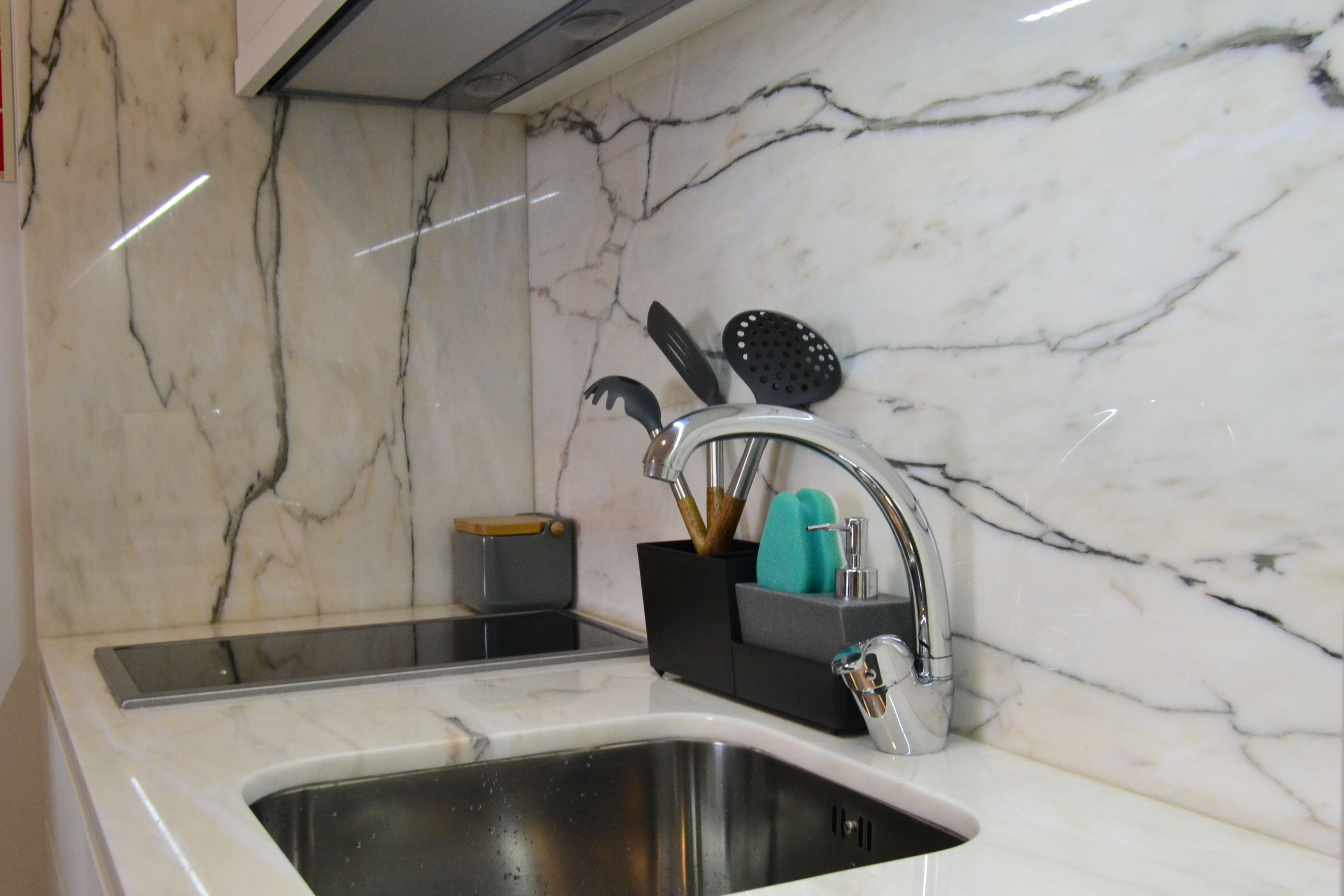 A kitchen with a marble backsplash, stainless steel sink, and a knife block with utensils.