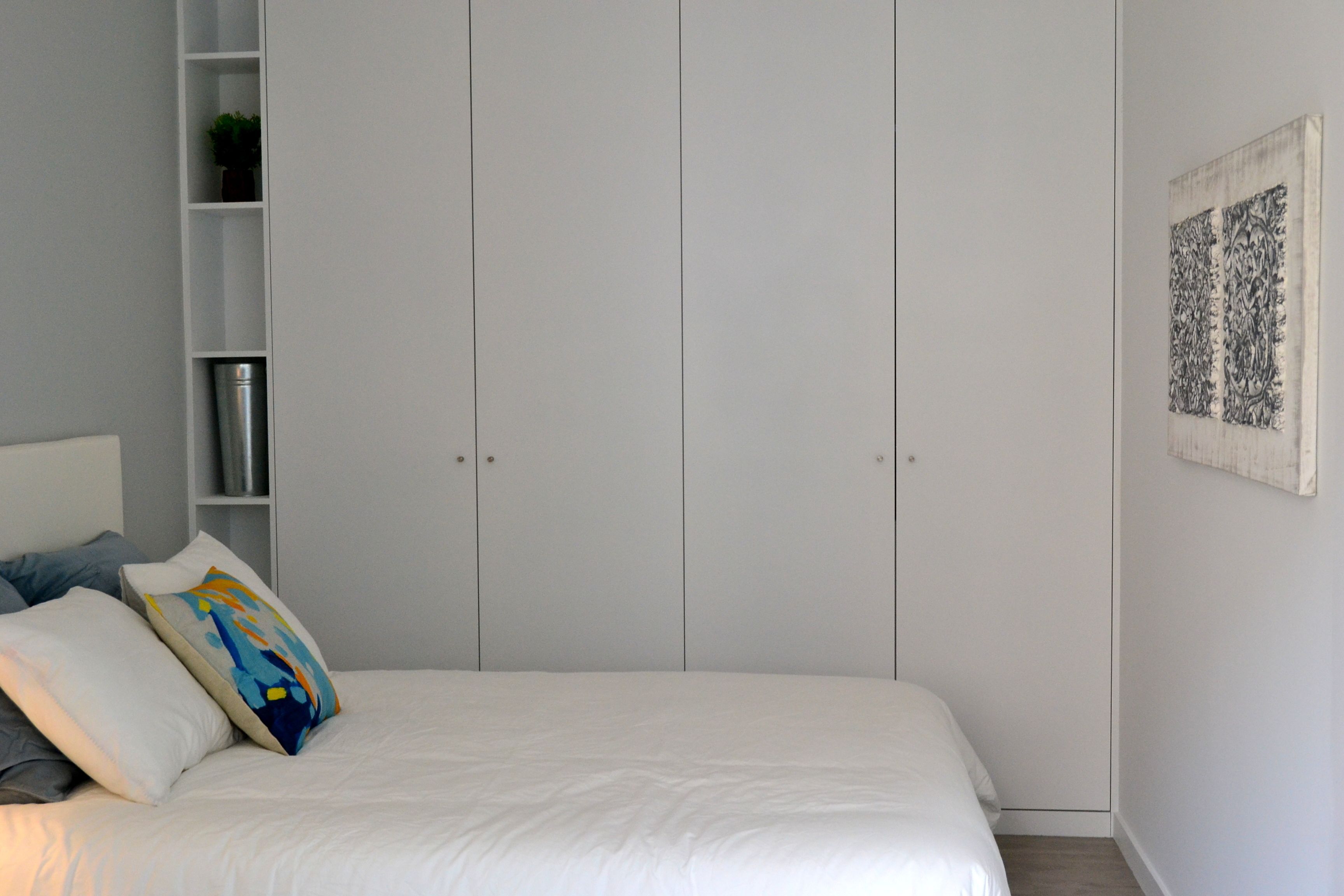 A bedroom with a bed, white walls, a wardrobe, and a framed artwork.