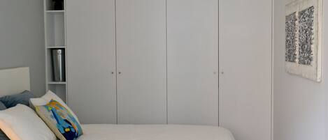 A bedroom with a bed, white walls, a wardrobe, and a framed artwork.