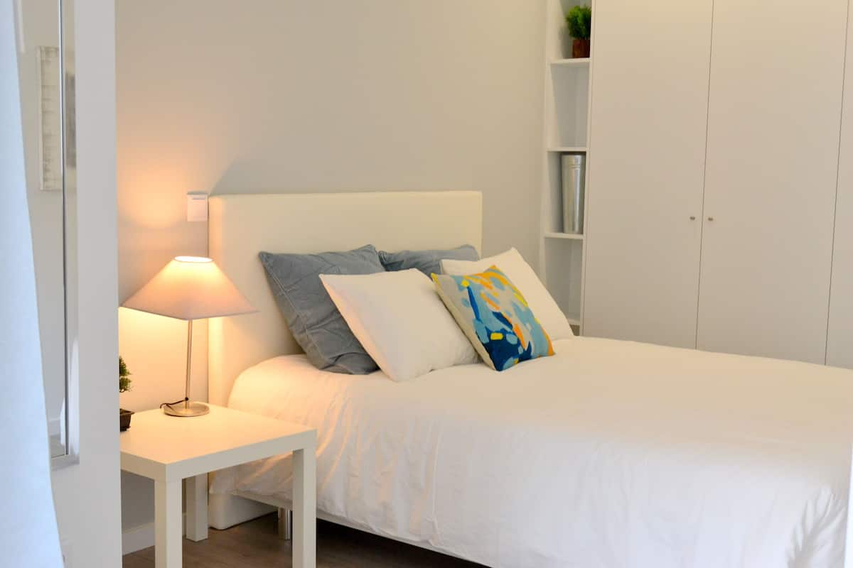 A neatly arranged bedroom with a bed, a bedside table with a lamp, and a wardrobe.