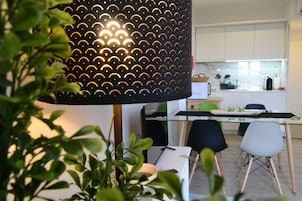Uma cozinha moderna com armários brancos, uma mesa de jantar de vidro e uma luminária pendente preta.