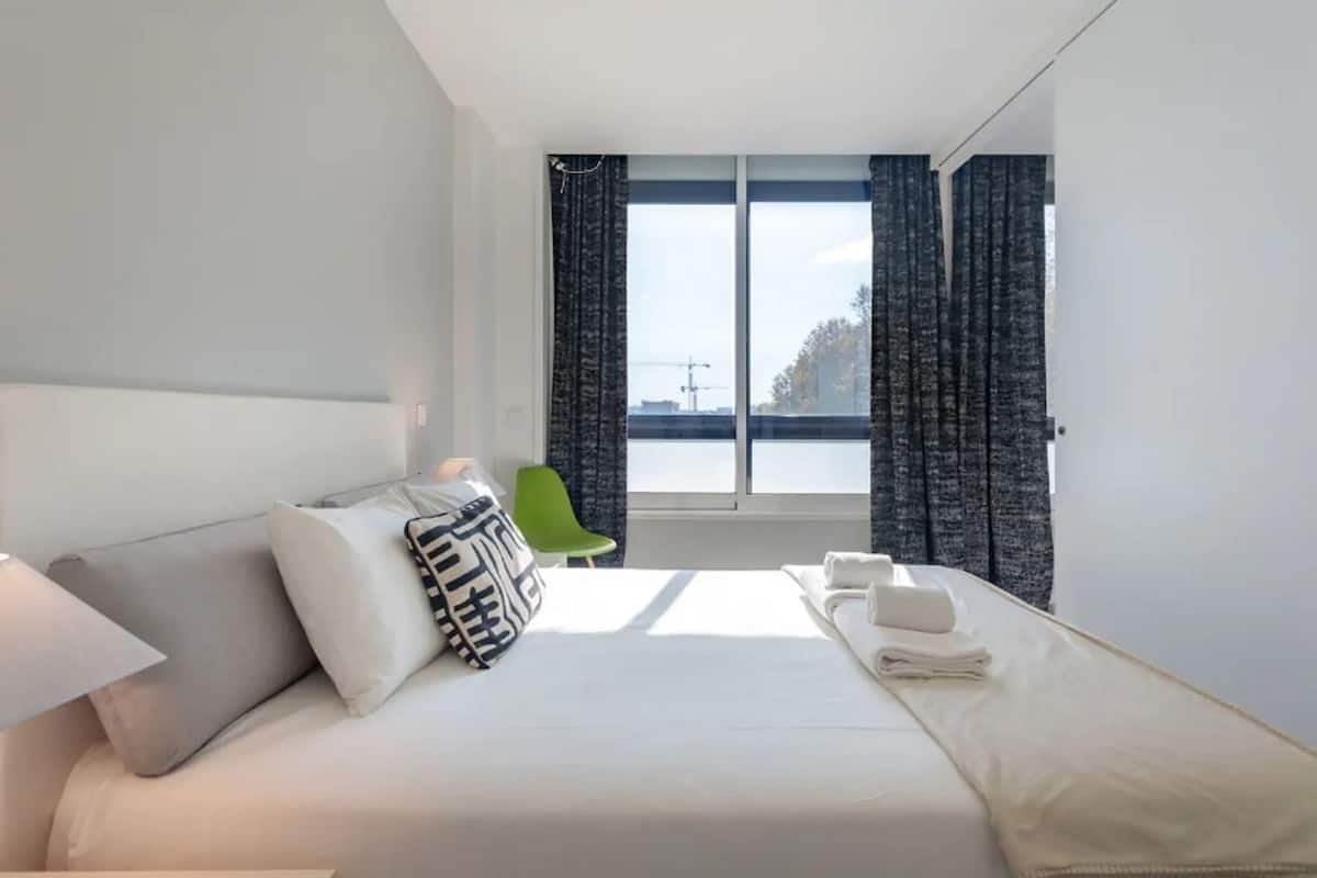 A modern hotel room with a large bed, a green chair, and a view of the city through the window.