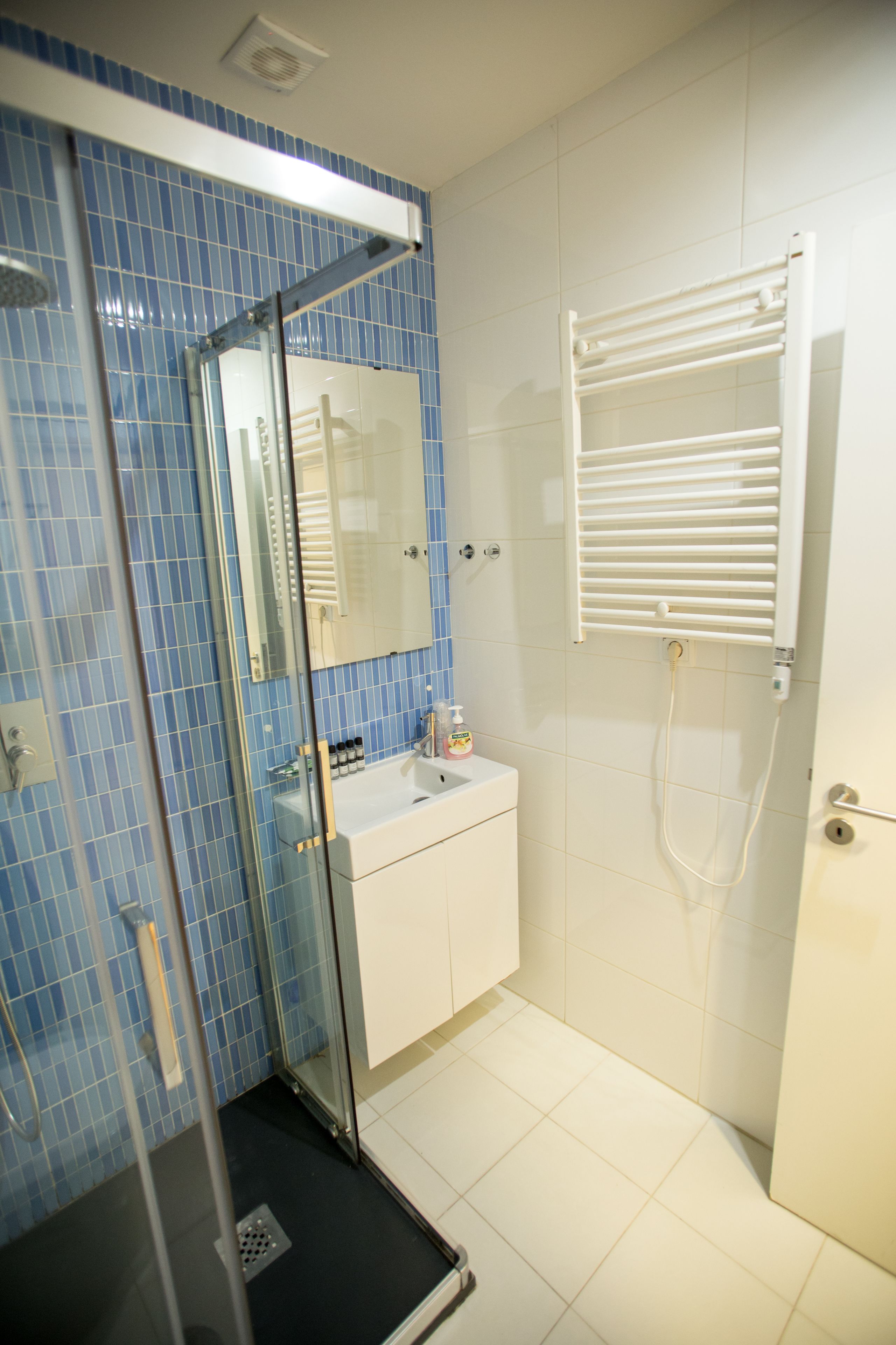 Un baño con cabina de ducha de vidrio, un lavamanos blanco y un perchero para toallas.