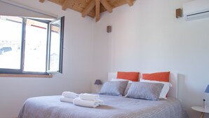 A bedroom with a wooden ceiling, a large bed with striped bedding, two pillows, and a bedside table with a lamp.