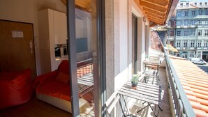 A balcony with a wooden ceiling, a red sofa, a dining table, and a view of buildings.