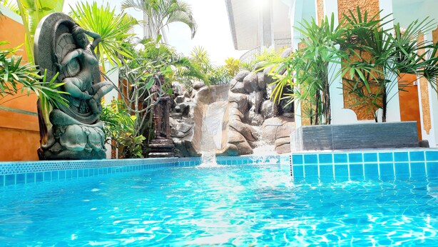 A swimming pool with a waterfall feature, surrounded by tropical plants and a stone statue.