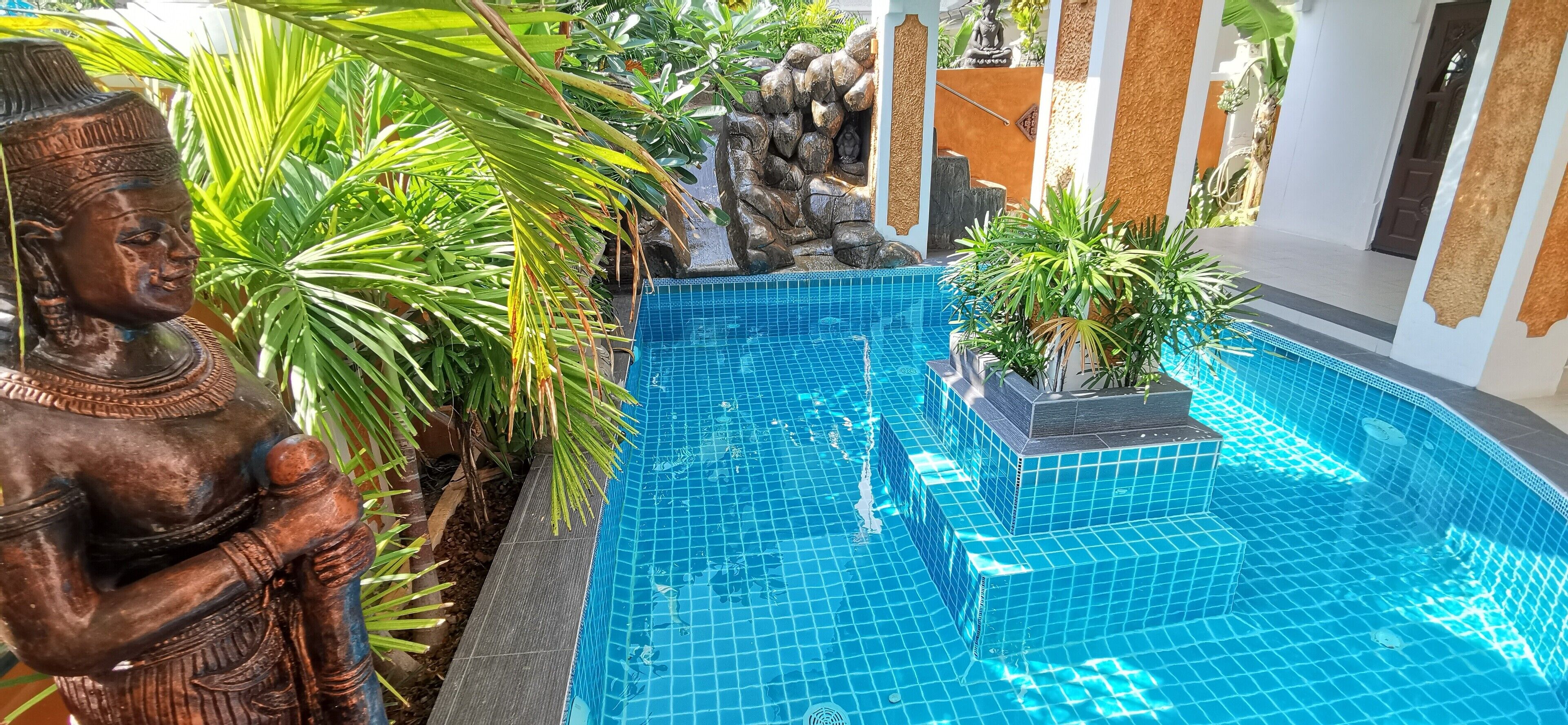 Una piscina con azulejos azules, rodeada de plantas y una estatua de Buda.