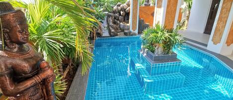 Una piscina con azulejos azules, rodeada de plantas y una estatua de Buda.