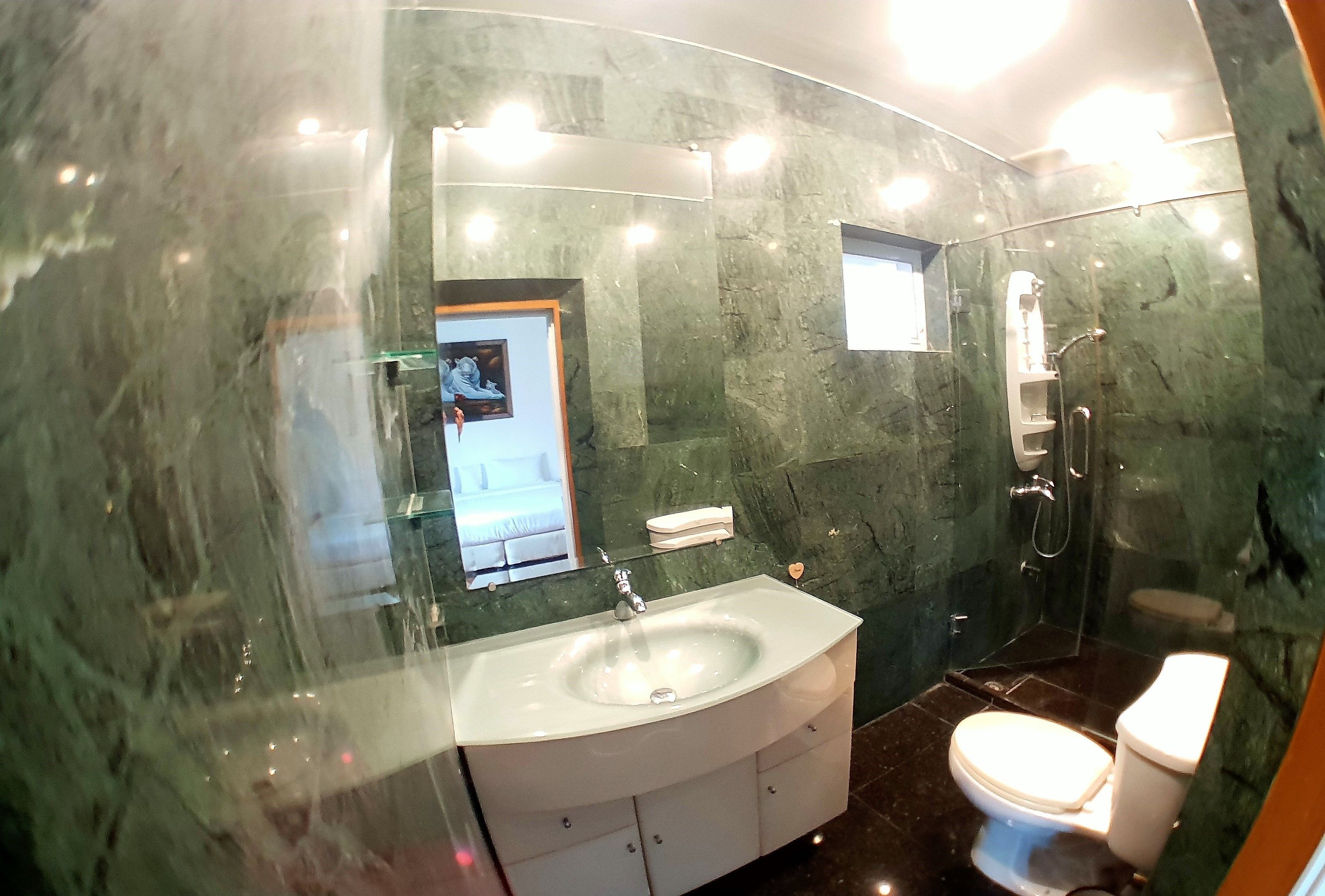 A bathroom with a marble wall, a sink, a toilet, and a shower.