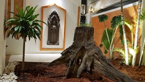 A room with a large tree stump centerpiece, a framed sculpture, and a potted plant.