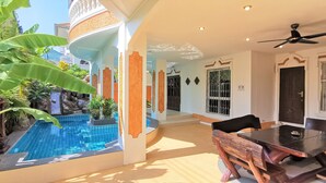 A poolside area with a dining table and chairs, a ceiling fan, and a view of a swimming pool.