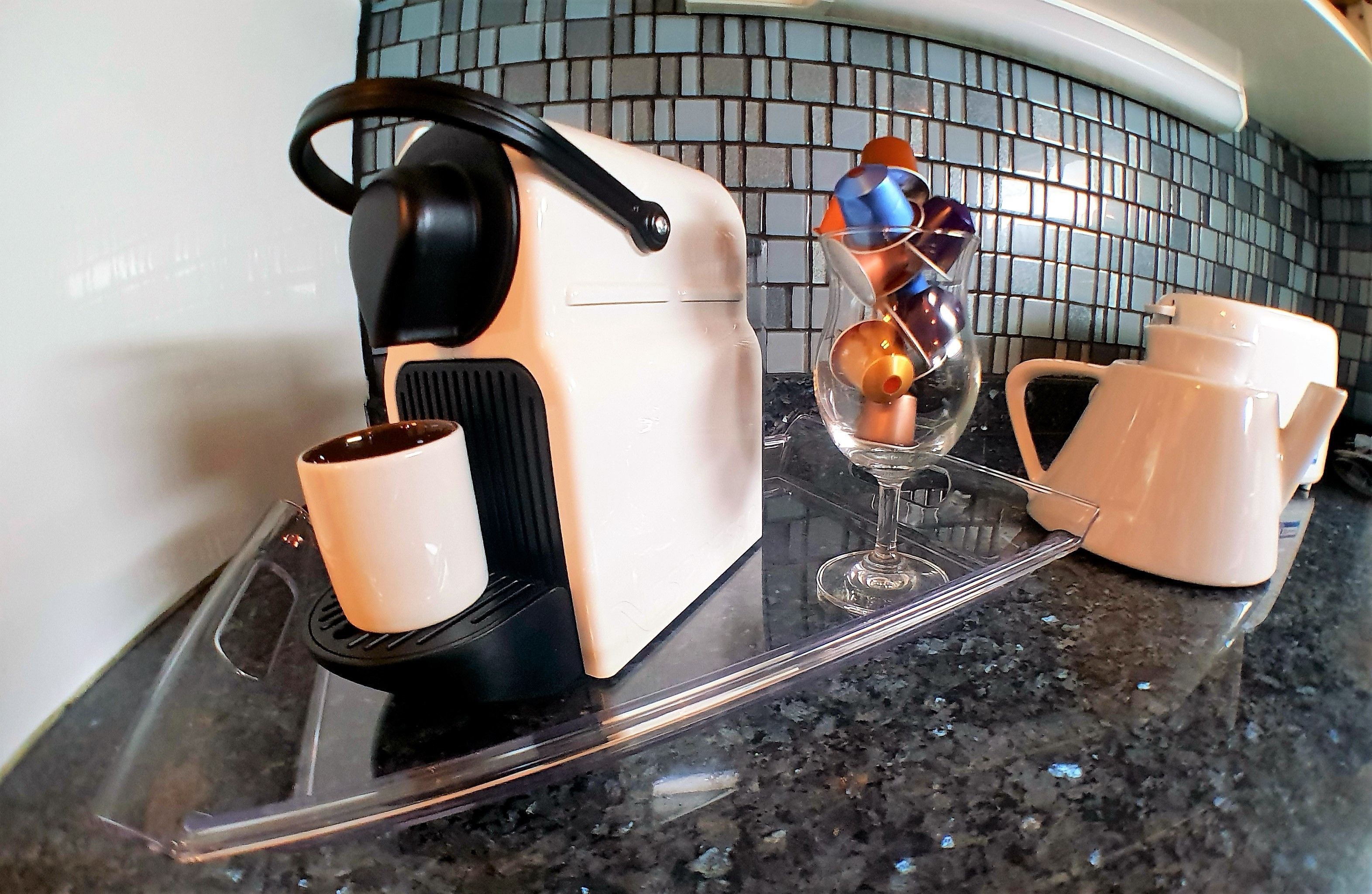 Una encimera de cocina con una cafetera, una copa de vino y una tetera.