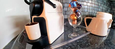 Una encimera de cocina con una cafetera, una copa de vino y una tetera.