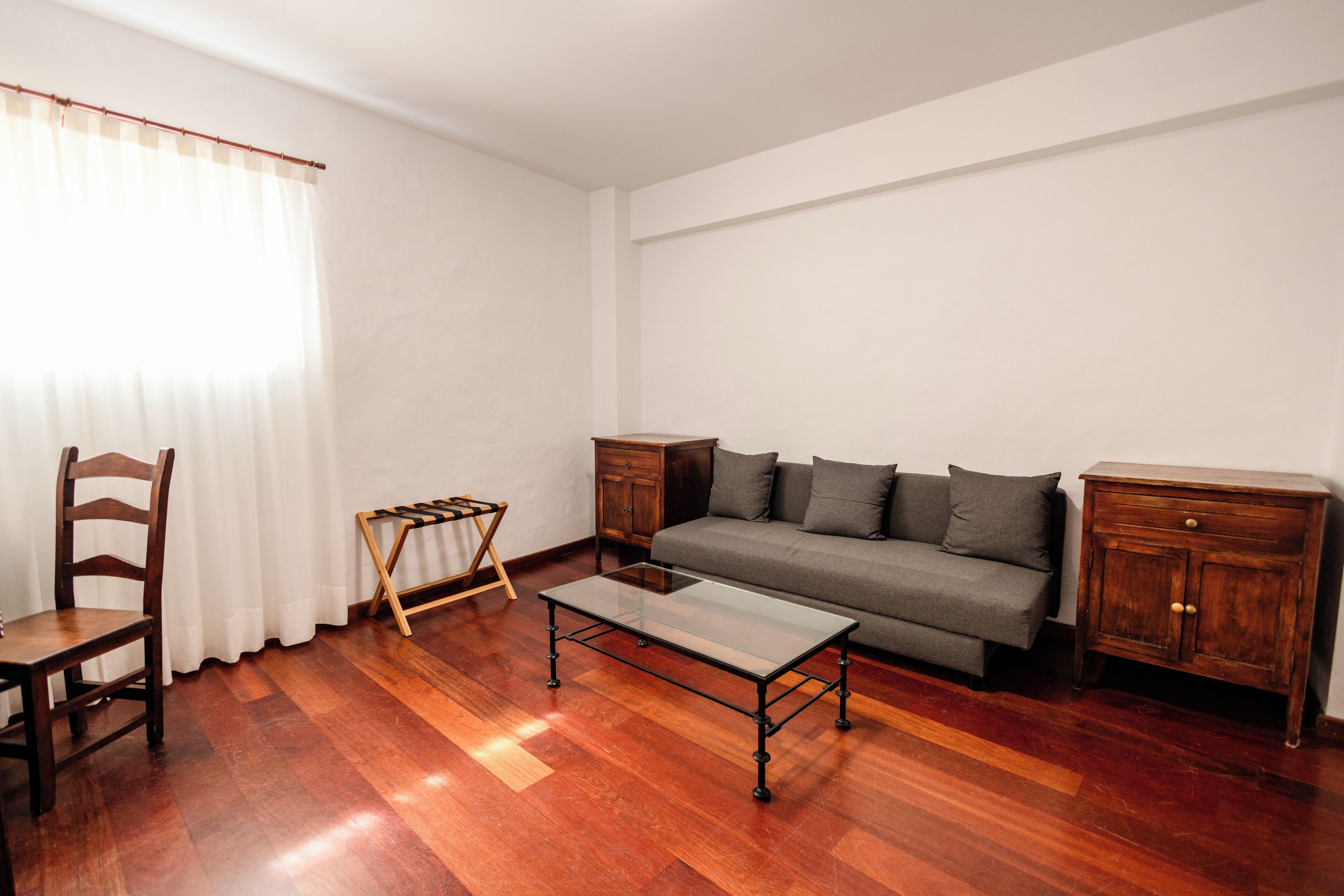 Een woonkamer met een bank, een houten stoel, een salontafel met glazen blad en een houten kast.