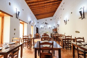 A dining area with wooden tables and chairs, stone wall decorations, and wall-mounted lighting fixtures. - Hotel Rural Casa de los Camellos (Aguimes)