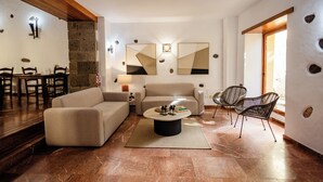 A modern living room with a sofa, armchairs, a coffee table, and a dining area with chairs. - Hotel Rural Casa de los Camellos (Aguimes)