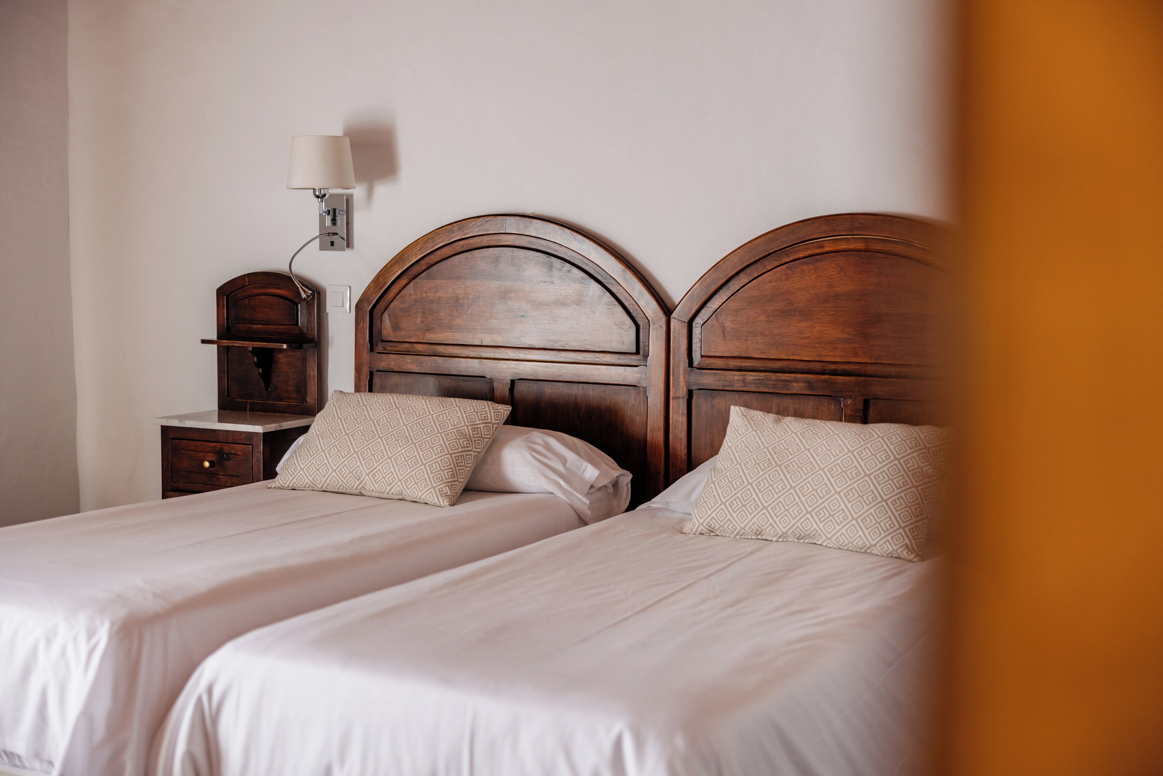 Un lit double avec une tête de lit en bois, une table de chevet et une lampe fixée au mur.