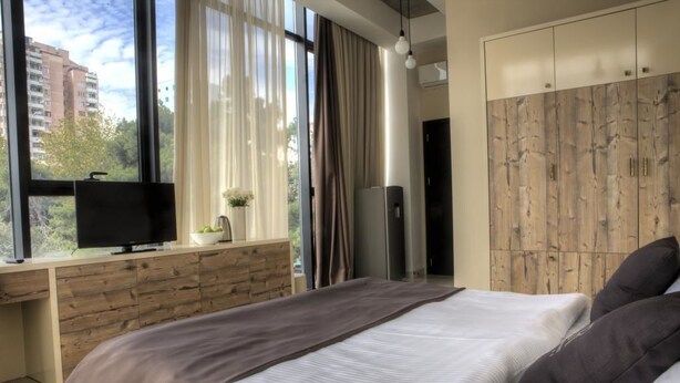 A modern bedroom with a large bed, a TV on a wooden desk, and a wardrobe. - Villa Residence Hotel (Tbilisi)