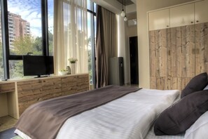 Une chambre moderne avec un grand lit, un téléviseur posé sur un bureau en bois et une armoire.