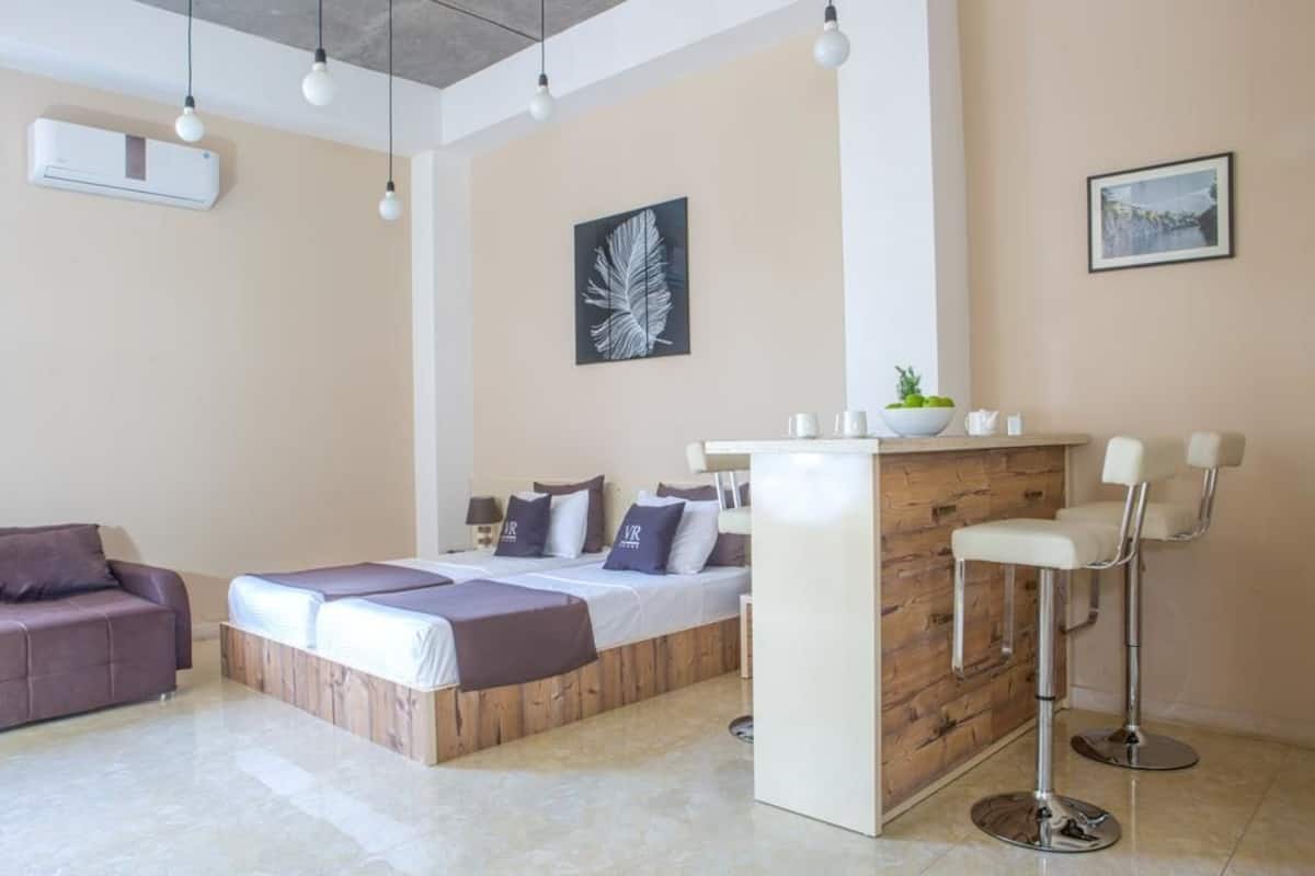 A modern bedroom with a bed, a sofa, a bar area, and a dining table.