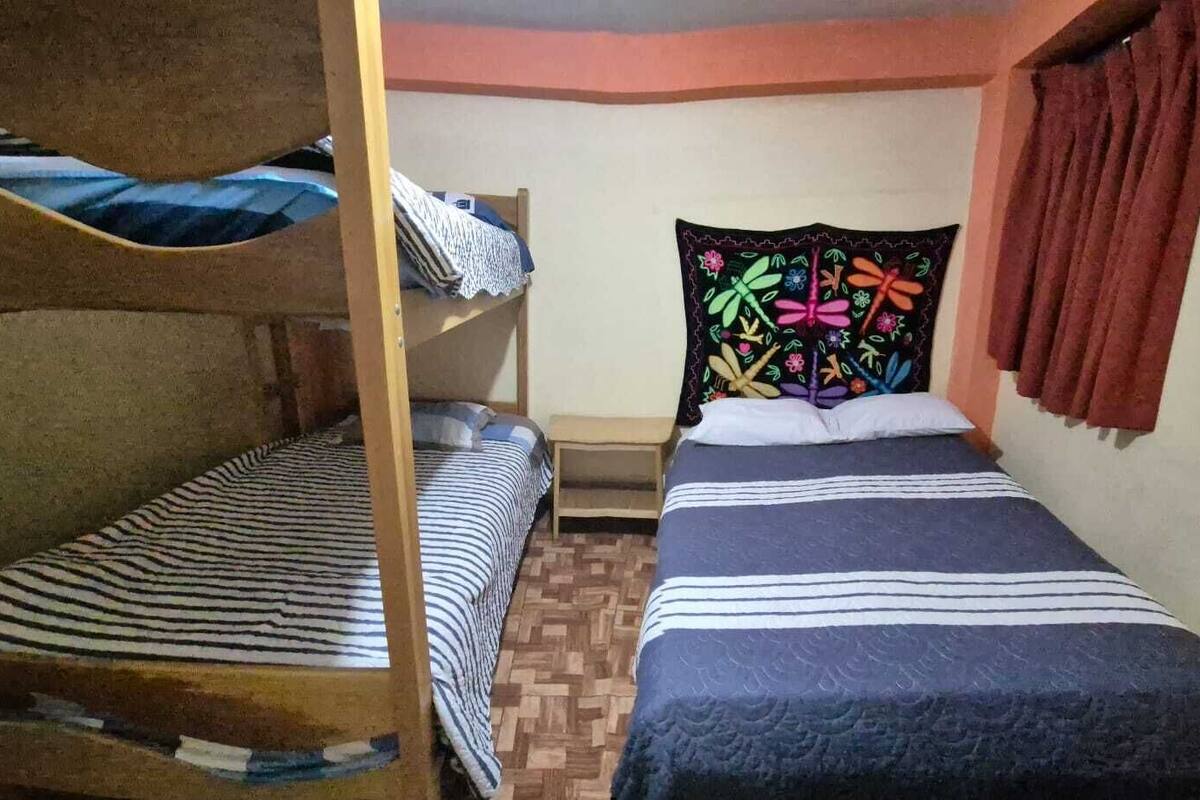 Ein Schlafsaalzimmer mit Etagenbetten, einem Einzelbett mit farbenfrohem Blumenkopfstück und einer kleinen Holzbank.