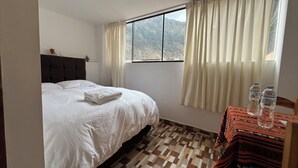Una habitación de hotel con cama, ventana con cortinas, una mesa con botellas de agua y un piso con diseño.