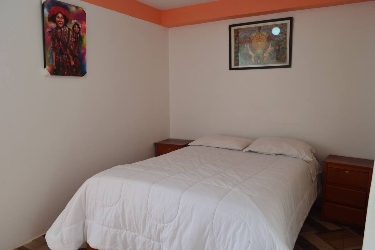 Ein Schlafzimmer mit einem Bett, zwei Nachttischen, einer weißen gesteppten Bettdecke und zwei gerahmten Bildern an den Wänden.